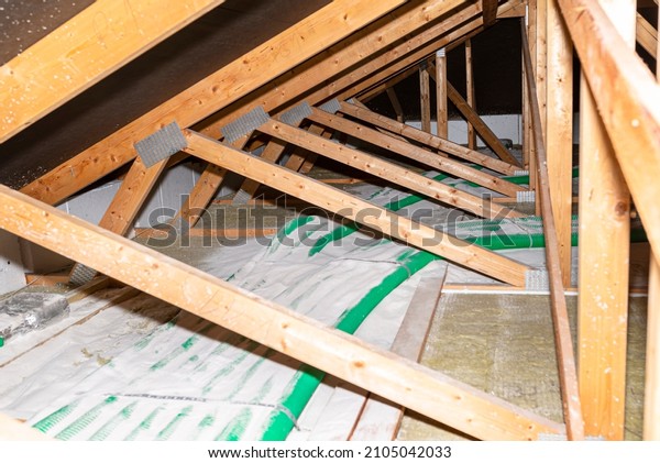 Pipe insulation with expanded perlite in\
domestic ventilation with energy recovery, a visible system of\
green pipes spread over the roof\
trusses.