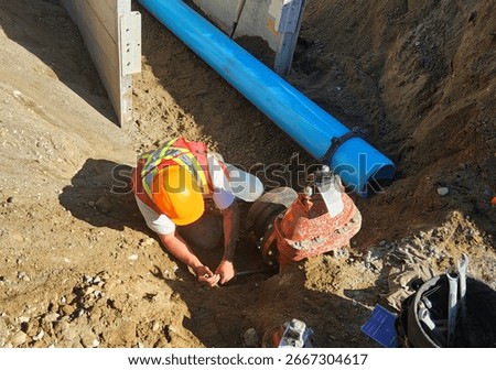 Pipe layer securing a flange-to-hub adapter onto a gate valve to connect a new PVC water main pipe section during underground utility installation.