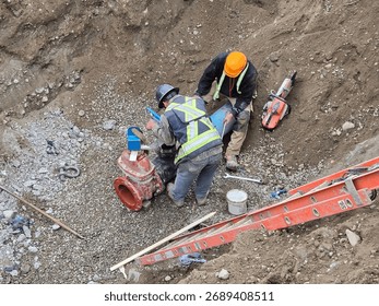 Pipe layers install new hydrant assembly with ductile iron fittings and flange connection inside trench during municipal watermain upgrade project.
