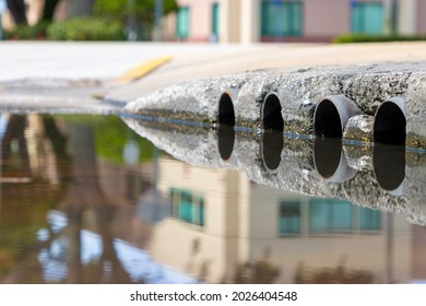 Pipe Openings To A Rain Water Flood Storm Drain Next To A Brown Puddle On A City Street