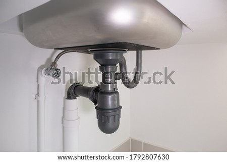 Pipe under kitchen sink. Consist of stainless steel, concrete counter, pvc plastic pipe, faucet, trap. Part of drainage and plumbing system. For water or sewer drain, siphon, repair and maintenance.