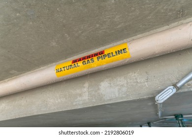 Pipe With Warning Natural Gas Pipeline Sticker Sign- San Antonio, Texas. Close-up Of A Pipeline With Warning Message On A Concrete Ceiling With Metal Pipes At The Back.