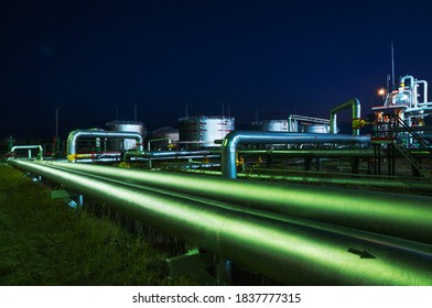 Pipelines in several rows and different configurations to a processing plant at night.