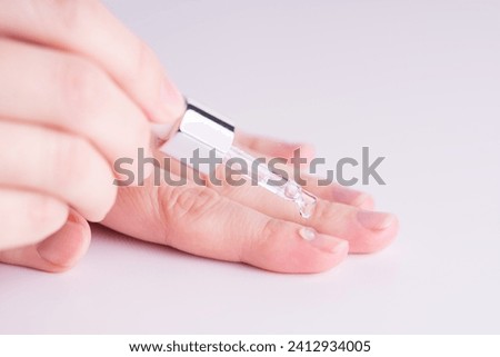 Pipette with a colorless drop of anti-brittle nails or oil for cuticles. The woman cares for hands and nails, close up. Woman applying oil from pipette to cuticle. Healthy nails concept, massage.