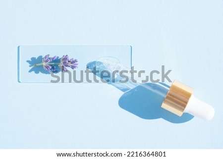 Pipette with cosmetic lavender oil over blue background. Texture of hydrolate or cosmetic oil with lavender extract for skin care. Selective focus