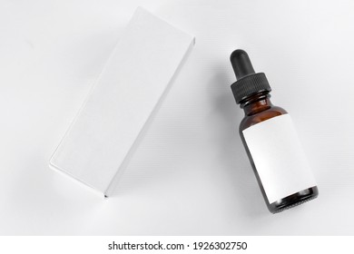 Pipette With Drop Of Cosmetic Oil Above Brown Bottle With Box