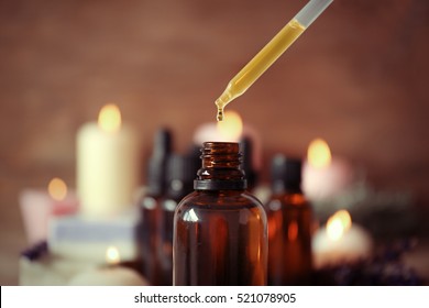 Pipette dropping essential oil into a glass bottle on blurred background