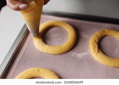 Piping choux pastry with a piping bag for making cream puff rings - Powered by Shutterstock