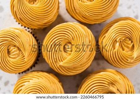 Piping dulce de leche buttercream frosting over vanilla cupcakes filled with caramel.