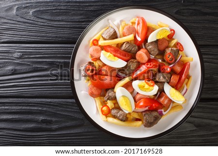 Pique macho is a Bolivian dish consisting of a layer of french fries buried underneath a heap of chopped beef, sausages, eggs, tomato, onions, peppers closeup. Horizontal top view from above
