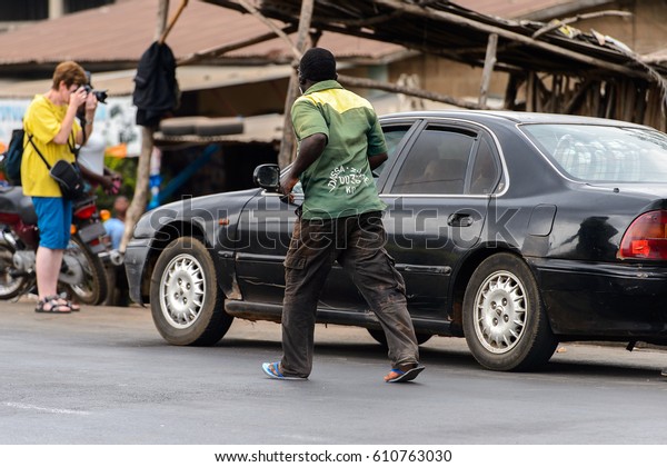 PIRA, BENIN - JAN 12, 2017: Unidentified\
Beninese man runs near the black car on the road . Benin people\
suffer of poverty due to the bad\
economy.