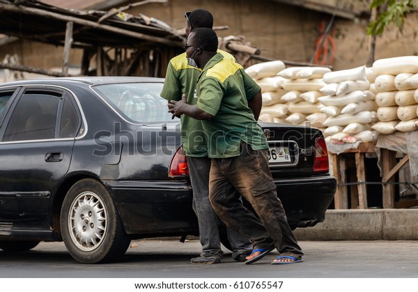 PIRA, BENIN - JAN 12, 2017: Unidentified\
Beninese two men stand near the black car on the road . Benin\
people suffer of poverty due to the bad\
economy.