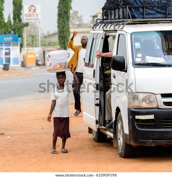 PIRA, BENIN - JAN 12,\
2017: Unidentified Beninese little girl carries a tray on her head\
near the white car. Benin children suffer of poverty due to the bad\
economy.