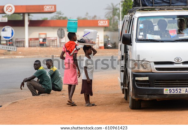 PIRA, BENIN - JAN 12, 2017: Unidentified\
Beninese people locate beside the road near the white car. Benin\
people suffer of poverty due to the bad\
economy.