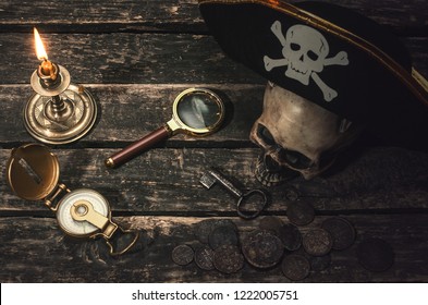 Pirate captain table with pirate hat on the human skull, compass, magnifying glass, mooring rope, coins, key of treasure chest and burning table. In the searching of gold.