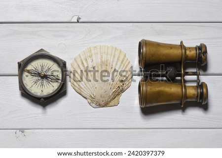 Pirate flat lay concept background. Binoculars, seashell and compass on the white wooden desk table background.