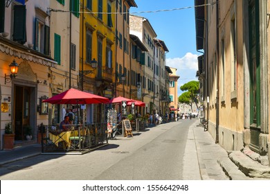 Pisa, Tuscany / Italy - August 16 2019: Street View Of Via Giosuè Carducci In The City Center Of Pisa With Ancient Building, Outdoor Café And The Town Walls In The Background In A Sunny Summer Day