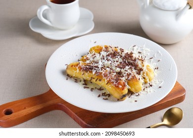 Pisang Bakar Coklat Keju or Grilled Banana Chocolate Cheese serve with chocolate sprinkles and cheddar cheese graters on white plate. - Shutterstock ID 2098450693
