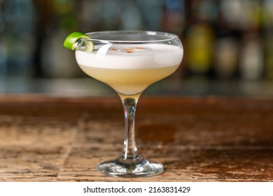 Pisco Sour cocktail on the bar. Blurred background. Peruvian, Mexican, Chilean traditional drink pisco sour liqueur with lime and egg. - Shutterstock ID 2163831429