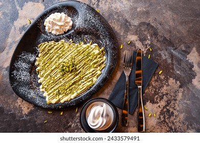 Pistachio Crepe With White chocolate with whipped cream, knife and fork served in dish isolated on dark background closeup top view of cafe baked dessert food - Powered by Shutterstock