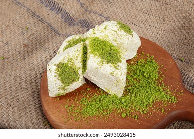 Pistachio halva (Halvah). Halva with pistachios on a rustic wooden table. Close-up of wooden plate with traditional Turkish pistachio halva and slices.