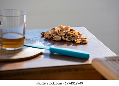 Pistachio nuts empty shells with turquoise knife on a small wooden table on a sunny terrace or balcony, hard light