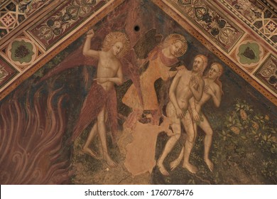 Pistoia, Italy - June 22, 2019: Late Gothic Garden Of Eden Fresco Depicting The Expulsion Of A Horrified Adam And Eve From Paradise By A  Cherubim Angel With Flaming Sword At The Church Of Tau