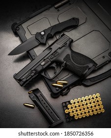 A pistol, cartridges for it and a folding knife on a dark background. Self-defense and survival kit. Compact edged weapons and firearms.