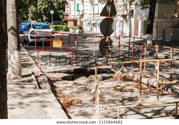 pit in asphalt pavement limited by\
fences. Asphalted on the road, the holes and pits due to its\
operation, a close-up of the\
infrastructure\
