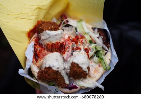 Pita sandwiches stuffed with crispy falafel, cool, crunchy tomatoes, cucumbers and onions and drenched with red sauce, close up, black background. Cheap but good dining in Paris Stock photo © 