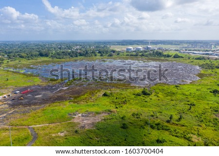 Pitch Lake, the liquid asphalt lake, the largest natural deposit of bitumen in the world.  La Brea, Trinidad island, Trinidad and Tobago. Natural asphalt mining and industrial trains of red minecarts.