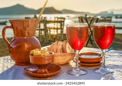 A pitcher and 2 glasses of sangria with side dishes in a Mediterranean restaurant at sunset