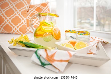 Pitcher and glasses of fresh fruit water on a tray with orange and green accents.