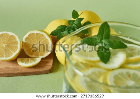 A pitcher of lemonade with fresh lemons and mint on a green background.