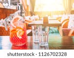 Pitcher with orange juice and two empty mugs stand on a table in a cafe on a hot, sunny day. Copy space for text.