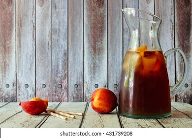 Pitcher of peach iced tea with fruit slices against a rustic wooden background
