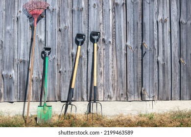 A Pitchfork, A Shovel, Against The Background Of A Wooden Wall Of A Horse Stable. Work Equipment On The Ranch