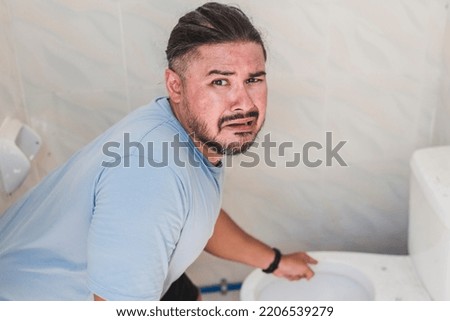 A pitiful man cringes and complains while pointing to a dirty toilet bowl. Public restroom problems.