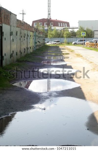 Pits with puddles on the road near the car\
garages. Summer and autumn background\
