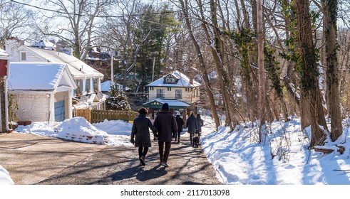 Pittsburgh, Pennsylvania, USA January 29, 2022 A group of people walking down a street next to a snow covered Frick Park on a sunny winter day in the Park Place neighborhood