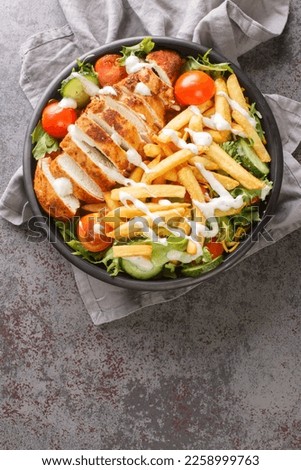Pittsburgh salad is a layered salad made of lettuce, vegetables, grilled meat, shredded cheese, riviera dressing, and French fries closeup on the bowl on the table. Vertical top view from above
