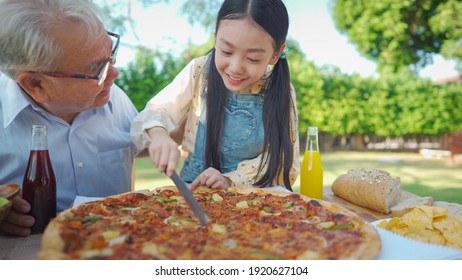 Pizza Being Cut By Asian Cute Girl And Her Uncle In Dinner Time At Garden. Asian Girl Using Kinfe Cutting Pizzas Severely For Her Uncle On A Special Family Day.