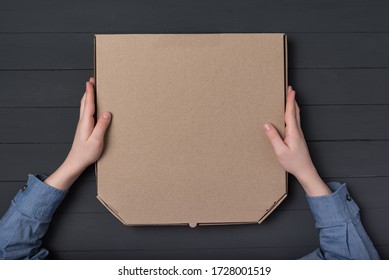 Pizza box in children's hands. Black background. Top view. Copy space.