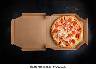 Pizza in a cardboard box against a dark background. Space for text. View from above. Pizza delivery. Pizza menu.