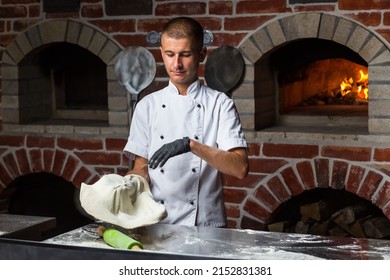 Pizza Chef Tossing Pizza Dough In The Air In A Traditional Pizzeria Kitchen