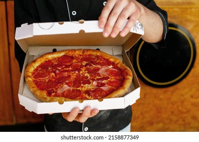 Pizza Chef Wearing Black Apron Holding Freshly Baked Pizza In Open Box At Pizza Shop Pizzeria