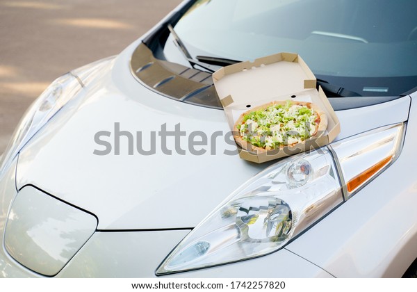 Pizza\
closeup on hood of the eco car. Safe delivery of pizza with green\
salad, tomatoes, cheese. Advertise in social network for restaurant\
delivery. Ecological delivering by electric\
car