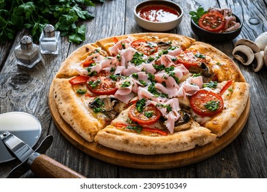 Pizza with cooked ham, mozzarella cheese and vegetables on wooden table