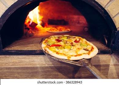 Pizza cooking in a traditional brick wood oven.Brick oven pizza on the wooden holder going to bake.Colorful vegetarian vegetable pizza baking 