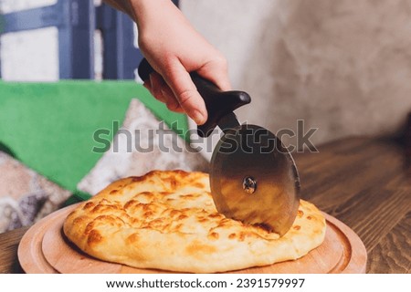 Pizza cutter wheel slicing ham pizza with capsicum and olives on wooden board on table